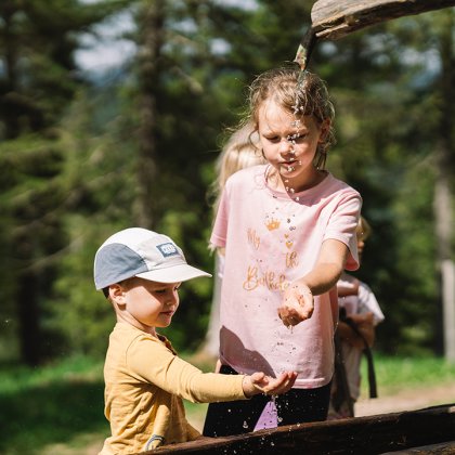 Children catching water flowing from a wooden pipe in the forest
