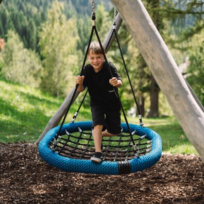 Child playing on a blue nest swing in a forest with mountains behind