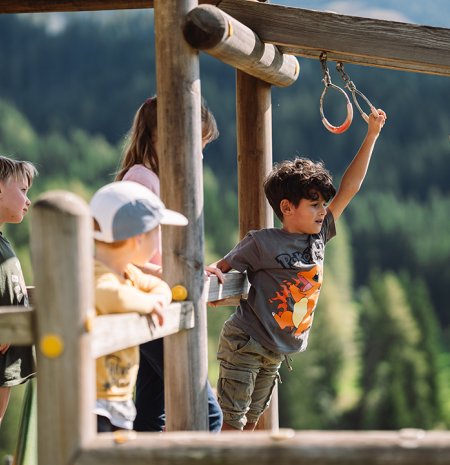 Children playing on a wooden playground with rings against a forested mountain background