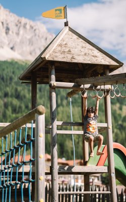 Child hanging from rings on a wooden playground structure with mountains behind