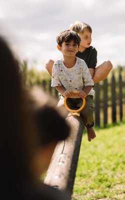 Zwei Kinder sitzen auf einer Wippe im Freien, eines hält ein gelbes Griffstück