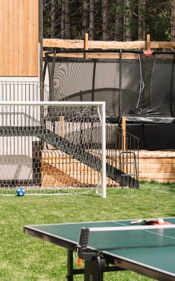 Soccer goal with blue ball on grass, trampoline and ping pong table in the garden background