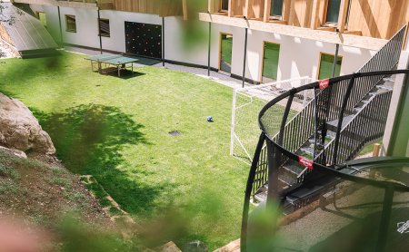 Blick auf einen Garten mit Fußballtor, Tischtennisplatte und Kletterwand neben einem Holzgebäude