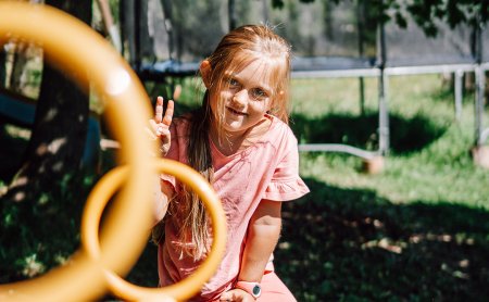 Bambina sorride e fa il segno di pace vicino a anelli gialli da arrampicata.