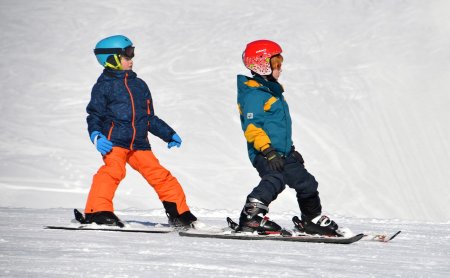 Kinder lernen Ski fahren auf Schnee mit bunter Kleidung und Schutzhelmen.