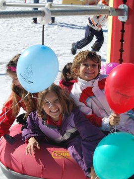 Fröhliche Kinder, die auf einem roten Snowtube mit bunten Luftballons im Schnee Spaß haben.