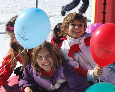 Happy children having fun on a red snow tube with colorful balloons in the snow.