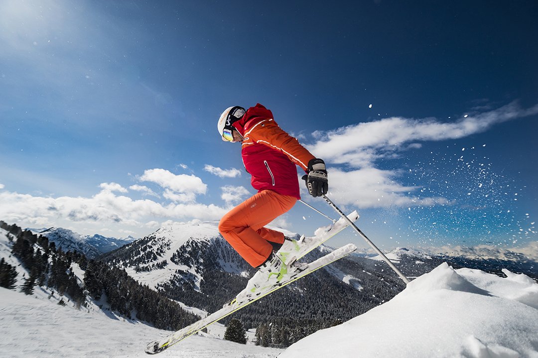 Skifahrer springt mit verschneiten Bergen und blauem Himmel.