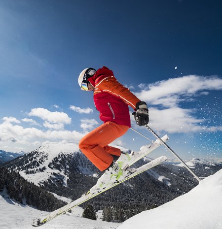 Skifahrer springt mit verschneiten Bergen und blauem Himmel.