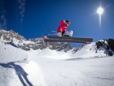 Mädchen springt mit Skiern auf einer verschneiten Piste an einem sonnigen Tag.
