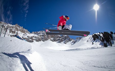 Mädchen springt mit Skiern auf einer verschneiten Piste an einem sonnigen Tag.
