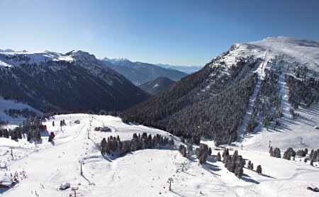 Verschneiter Berg mit Skipisten und Liften unter klarem Himmel.