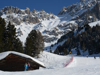 Schnee, kleine Holzhütte, Kinder in Skikleidung, Berge im Hintergrund.