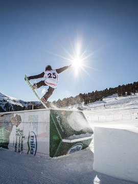 Junge Snowboarder macht Trick auf Hindernis im sonnigen Snowpark.