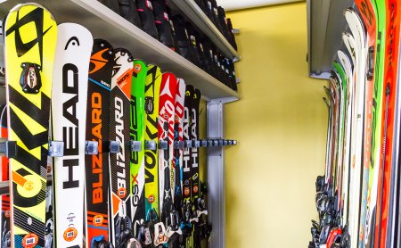 Skier stehen ordentlich aufgereiht in einem Skiraum an Wandhaltern.
