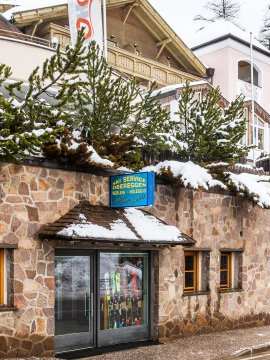 Steinernes Skiverleih-Geschäft mit Skiern hinter einer Glastür, Schnee.