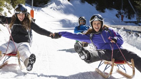 Due donne sorridenti slittano mano nella mano giù per una collina innevata.