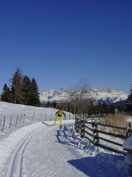 Langläufer auf präparierter Loipe mit verschneiter Landschaft und Bergen.