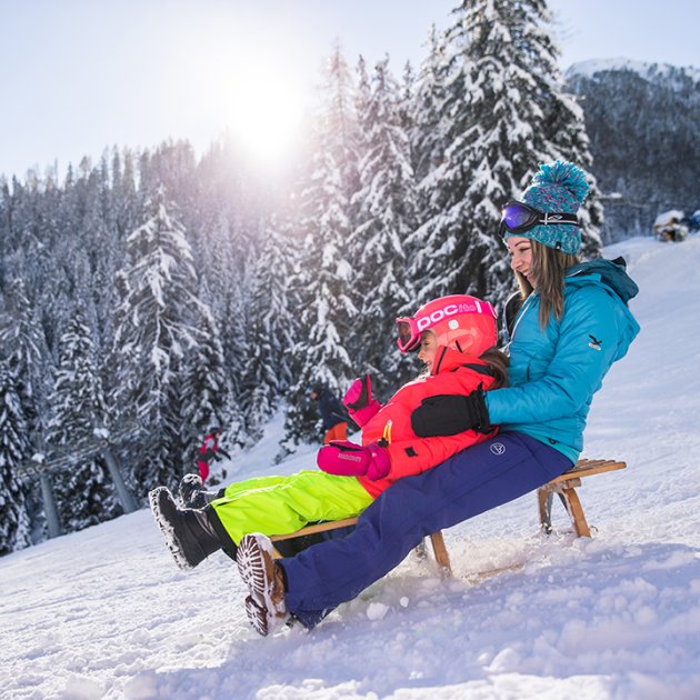 Due ragazze sorridenti scendono in slitta sulla neve.