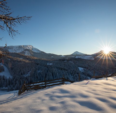 Sonnenuntergang über verschneiter Landschaft mit Bäumen und Bergen.