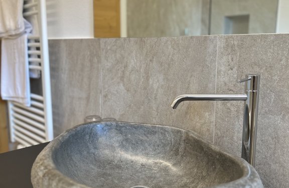 Badezimmer-Waschbecken aus Stein mit silbernem Wasserhahn und Handtüchern