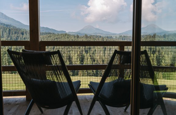 Zwei Stühle auf einem Balkon mit Blick auf bewaldete Berge und blauen Himmel