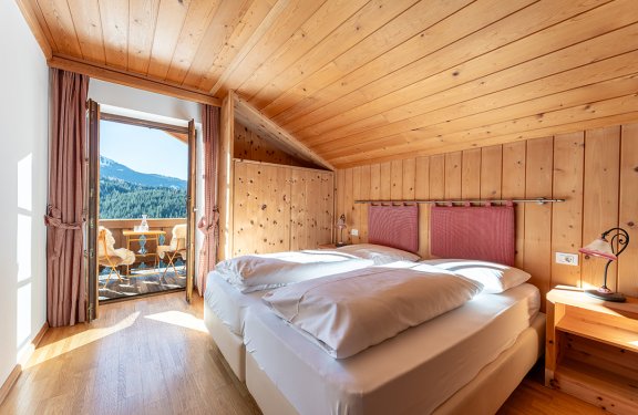 Gemütliches Zimmer mit Doppelbett, hellem Holz und sonnigem Balkon.