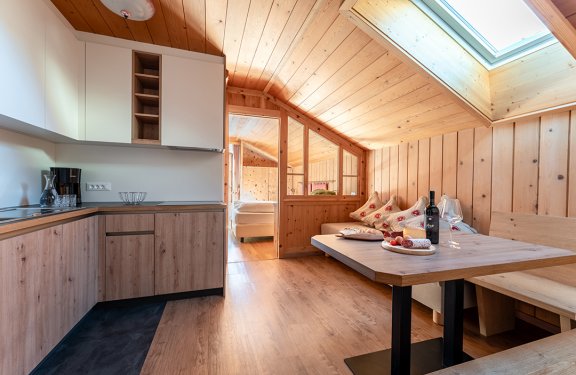Wohnbereich mit Küchenzeile, Holztisch und Sofa mit Kissen.