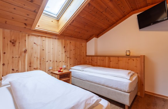 Einzelzimmer mit zwei Betten und Holzwänden, Dachfenster und Holzfußboden
