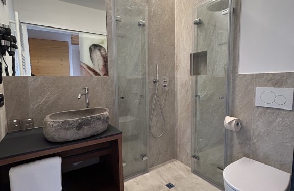 Modernes Badezimmer mit Glasdusche, grauen Fliesen und steinernem Waschbecken