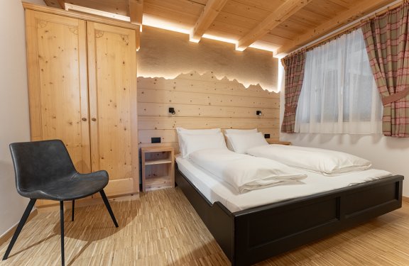 Schlafzimmer mit Doppelbett, Holzschrank, schwarzem Stuhl und Fenster mit karierten Vorhängen