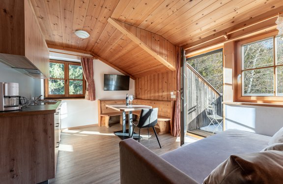 Heller Wohnbereich mit Küche, Essplatz und Sofa, offene Tür zum Balkon