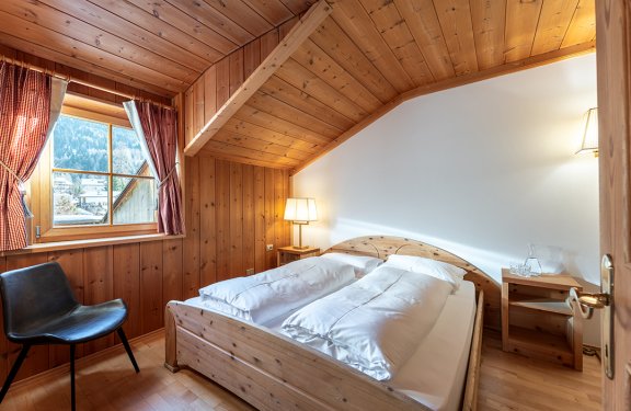 Holzschlafzimmer mit Doppelbett, Stuhl und Fenster mit Vorhängen