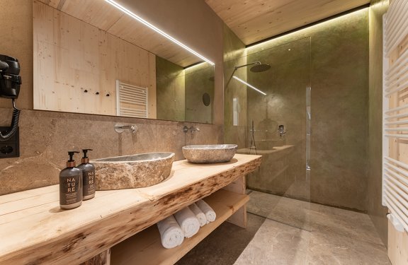 Modern bathroom with two stone sinks, wooden countertop, and walk-in shower