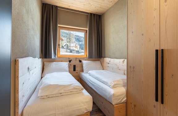 Twin bedroom with wooden beds and window showing mountain and house view