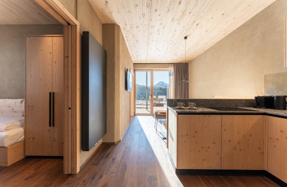 View down a hallway with wooden floor to a terrace with mountain view, bedroom on left, kitchen on right