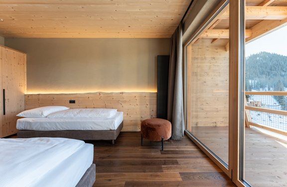 Modern bedroom with two beds on the left, wood paneling, and large window on the right showing mountain view