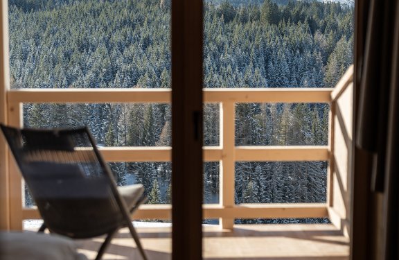 View through glass door to balcony with chair and snowy mountain landscape