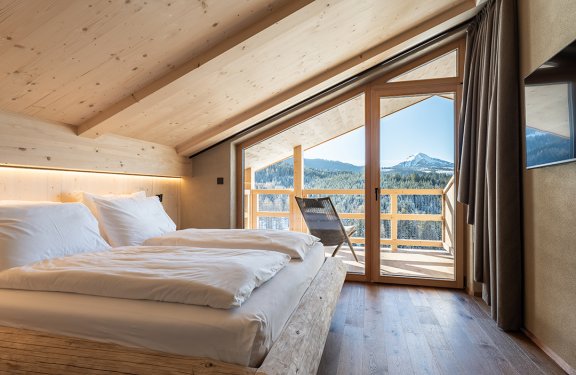 Bedroom with wooden bed and balcony chair overlooking mountain landscape