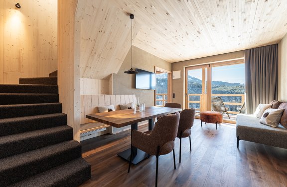 Bright living room with wooden table, chairs, sofa, and balcony overlooking mountains