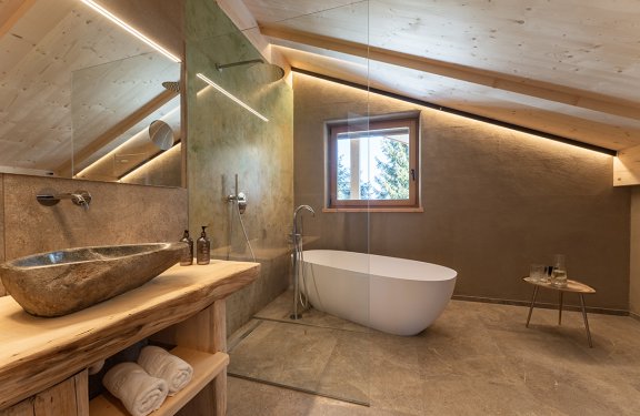 Modern bathroom with freestanding bathtub, stone sink, and wooden ceiling under sloped roof