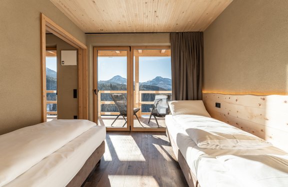 Helles Zimmer mit zwei Einzelbetten und Balkon mit Bergblick bei Sonnenschein