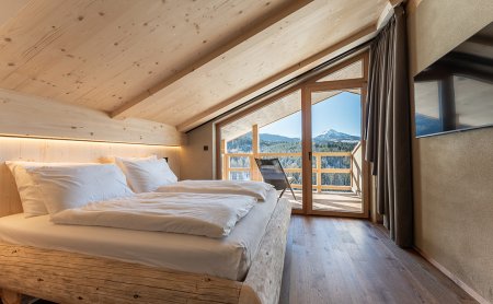 Schlafzimmer mit Holzbett links und Balkon mit Bergblick rechts