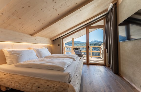 Bedroom with wooden bed on left and balcony with mountain view on right