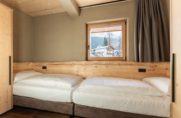 Two single beds side by side in a room with wood paneling and a window showing mountain view