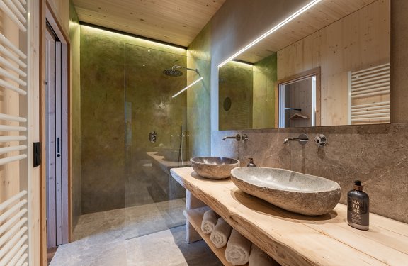 Modern bathroom with stone sinks, wooden countertop, and walk-in shower with glass panel