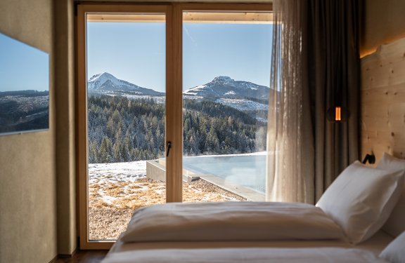 View from a bedroom window of snowy mountains and forest under clear sky