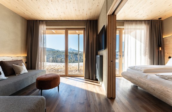 Modern hotel room with sofa on left, bed on right, and mountain view through large windows